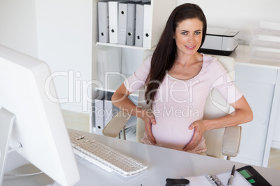 Casual pregnant businesswoman touching her bump at her desk smil