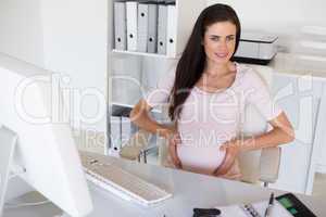 Casual pregnant businesswoman touching her bump at her desk smil