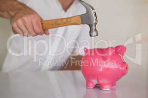 Casual businessman breaking piggy bank with hammer