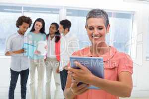 Businesswoman looks at tablet pc while coworkers stand behind he