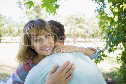 Pretty blonde smiling at the camera in a park while hugging boyf