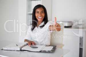 Pretty businesswoman showing thumb up to camera at her desk