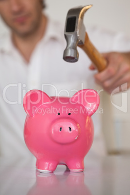 Casual businessman breaking piggy bank with hammer