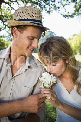 Smiling man offering his girlfriend a white flower in the park