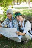 Active smiling couple sitting down on a hike holding map