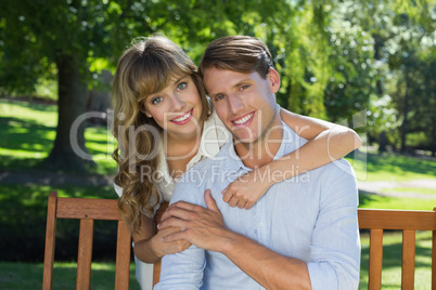 Affectionate couple relaxing on park bench together smiling at c