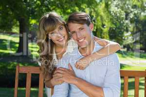 Affectionate couple relaxing on park bench together smiling at c