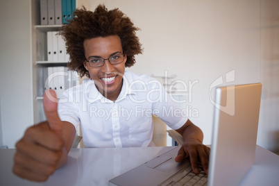 Casual businessman smiling at camera at his desk showing thumbs