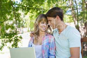 Smiling young couple sitting on park bench using laptop