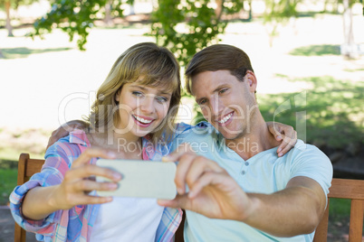 Smiling couple sitting on bench in the park taking a selfie