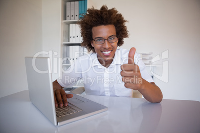 Casual businessman smiling at camera at his desk showing thumbs