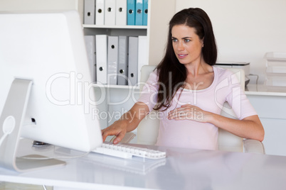 Casual pregnant businesswoman touching her bump at her desk