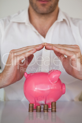 Casual businessman sheltering piggy bank and coins