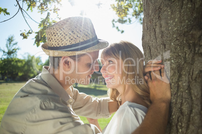 Cute smiling couple leaning against tree in the park