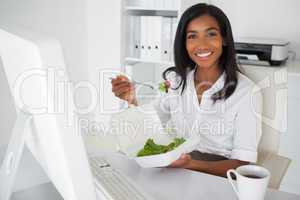 Smiling businesswoman eating a salad at her desk