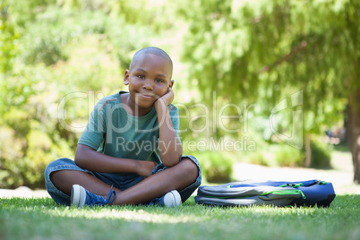 Happy schoolboy smiling at camera sitting on grass