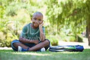 Happy schoolboy smiling at camera sitting on grass