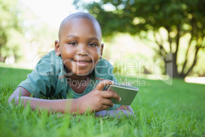 Little boy lying on grass holding digital camera smiling at came