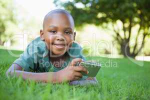 Little boy lying on grass holding digital camera smiling at came