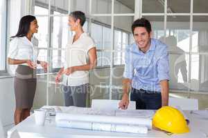 Architect smiles at camera while coworkers stand in background