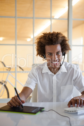 Casual young businessman using digitizer and headset at desk