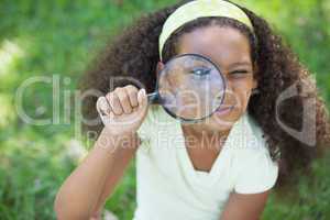 Young girl looking through magnifying glass in the park