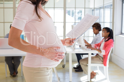 Pregnant office worker touches bump and reads document