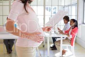 Pregnant office worker touches bump and reads document