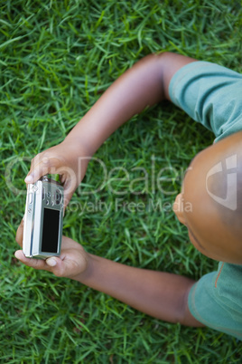 Little boy lying on grass looking at digital camera