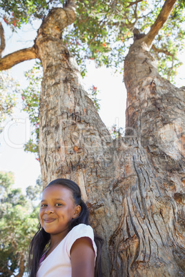 Little girl sitting by large tree smiling at camera