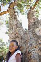 Little girl sitting by large tree smiling at camera