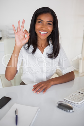 Pretty businesswoman making ok sign to camera at her desk