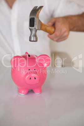 Casual businessman breaking piggy bank with hammer