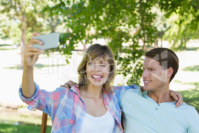 Cute couple sitting on bench in the park taking a selfie