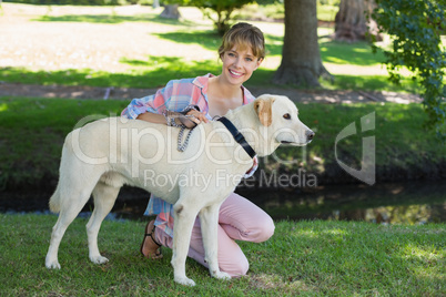 Pretty smiling blonde kneeling with her labrador in the park