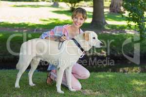 Pretty smiling blonde kneeling with her labrador in the park