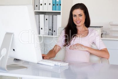 Casual pregnant businesswoman touching her bump at her desk smil