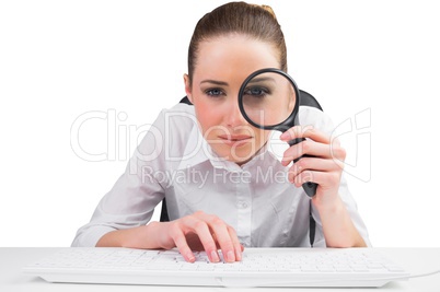 Businesswoman typing and looking through magnifying glass