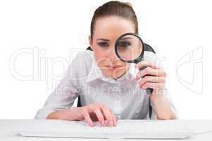 Businesswoman typing and looking through magnifying glass