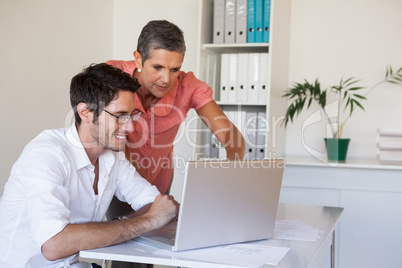 Casual business team working together at desk using laptop