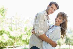 Carefree couple standing in the park and hugging smiling at came