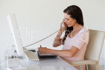 Casual pregnant businesswoman talking on phone at her desk