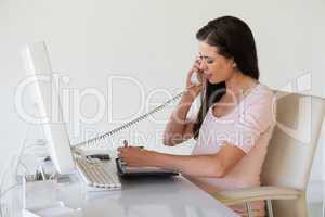Casual pregnant businesswoman talking on phone at her desk