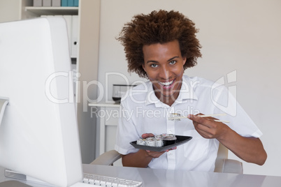 Casual smiling businessman eating sushi at his desk