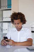 Casual businessman using his smartphone at his desk