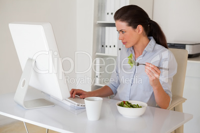 Casual brunette businesswoman eating a salad at her desk