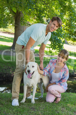 Happy couple with their labrador in the park smiling at camera