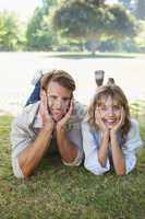 Carefree couple lying in the park smiling at camera