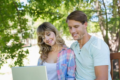 Cute young couple sitting on park bench using laptop