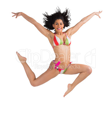 Fit girl in bikini leaping and smiling at camera